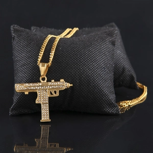 Gros plan détaillé du pendentif pistolet Uzi doré avec strass sur un coussin noir chic