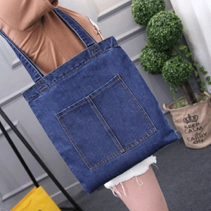 Large blue denim tote bag with front pocket shown worn over the shoulder