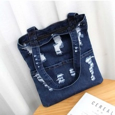 Detailed top view of a dark blue denim tote bag with distressed ripped details on wood