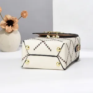 Detail view of cream handbag showing brown trim, diamond stitching and golden feet