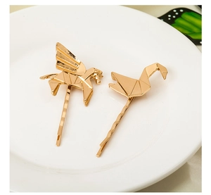 Close-up of golden geometric pegasus and origami crane metal hair clips on white tray
