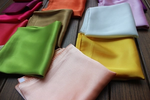 Detailed view of colorful satin square scarves with a silky texture on a wooden floor