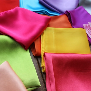 Vibrant folded satin square scarves in multiple colors on a dark wooden background