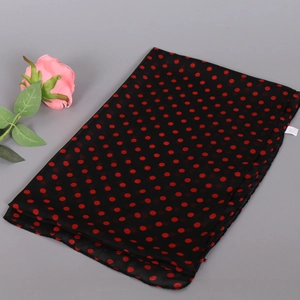 Flat lay of a black chiffon scarf with red polka dots and a pink rose on grey background