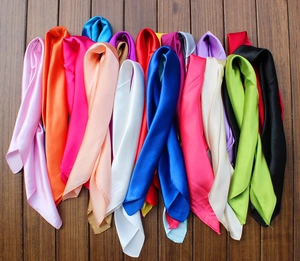 Detailed view of colorful square silk scarves stacked on a brown wooden floor surface