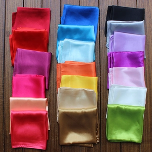 Macro shot of 20+ assorted solid color satin silk scarves neatly folded on a wood surface