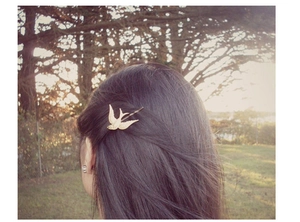 Golden swallow shaped metal hair clip worn on hair with a natural outdoor background