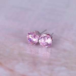 Close-up of pink round zircon earrings featuring six-prong setting on marble background