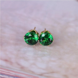Macro view of 8mm green zircon stud earrings with gold six-claw setting on marble