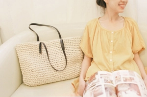 Close-up of large beige woven straw tote bag with brown handles in a casual setting