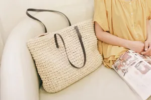Chic beige woven straw tote bag with brown leather straps on a sofa, bohemian beach style