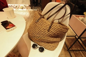 Large straw tote bag with brown leather straps displayed on a chair for summer vacation