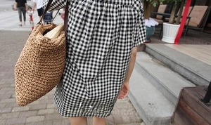 Detail of a large woven straw tote bag with rope handles and a checkered summer dress