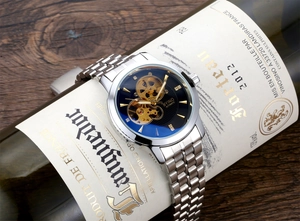 Macro shot of silver mechanical watch with blue hollow dial on premium red wine bottle