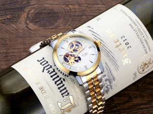 Close-up of automatic skeleton watch with two-tone metal strap on a wine bottle