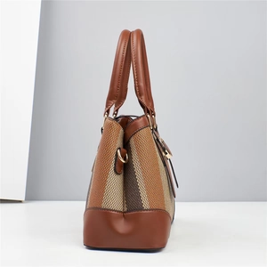Detail of a stylish woven handbag with brown leather handles and gold metal hardware