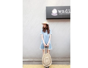 Detail of round hollow-out straw handbag with colorful pompoms on a sun hat and denim dress