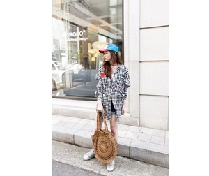 Outdoor street style showing a large round straw handbag paired with a plaid long shirt