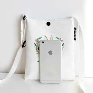 Mini white canvas crossbody bag with rabbit graphic shown next to phone for size reference
