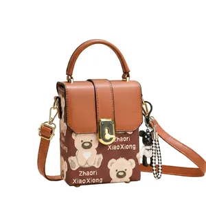 Detail of the brown flap handbag with bear pattern, metal lock, and plush charm