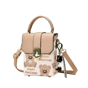 Detail of beige tote bag featuring cute bear pattern, metal lock, and bear charm accessory