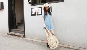 Detail of light blue denim mini dress featuring white fringe trim and summer straw bag