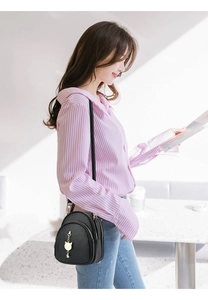 Close-up of black lychee grain leather mini bag with gold cat charm and zipper details