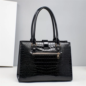 Detail of glossy black crocodile embossed faux leather handbag with gold metal zipper