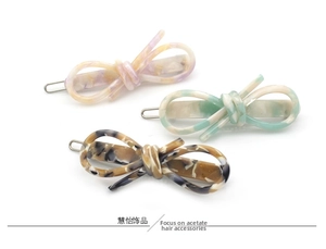Vue détaillée de trois barrettes à cheveux en acétate avec nœuds en rose, vert et écaille de tortue