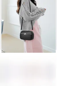 Detail of compact black pebble leather crossbody bag with dual silver zippers and slim strap