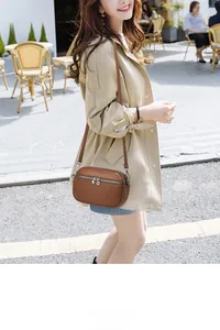 Detail of brown litchi grain leather texture and silver zippers on a crossbody camera bag