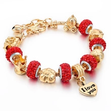 Detailed macro view of gold-plated snake chain bracelet with red crystal beads and charms