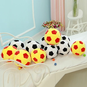 Pile of soft plush soccer pillows in red and yellow colors on a cozy white bed