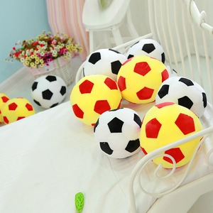 Soft plush soccer ball pillows in black, white, yellow and red on a cozy bed