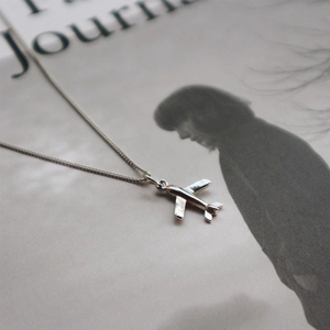 Artistic detail of a silver airplane pendant necklace placed over a fashion magazine
