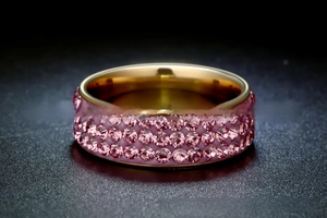 Macro detail of three rows of pink crystals paved on a gold stainless steel ring band