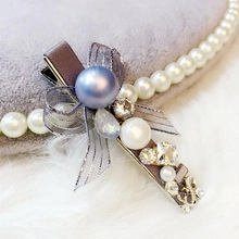 Dettaglio di fermaglio con perla blu opaca e fiocco in nastro grigio con strass