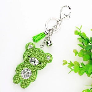 Detail of green rhinestone bear keychain with tassels and bell on a white surface