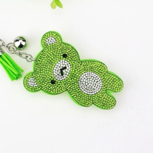 Macro detail of green rhinestone bear keychain featuring metallic bell and suede tassel