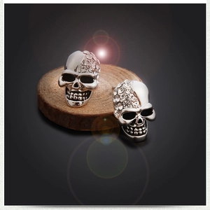 Gothic silver skull stud earrings with crystal rhinestones on a wooden stand