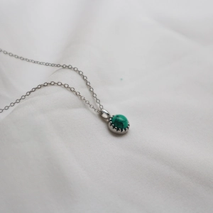 Macro detail of a silver S925 necklace with a round green turquoise pendant on white fabric
