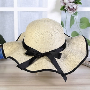Detailed view of beige straw sun hat with wide brim and elegant black ribbon bow tie