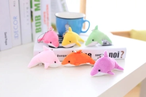 Mini porte-clés dauphins en peluche de six couleurs vives posés sur un livre blanc