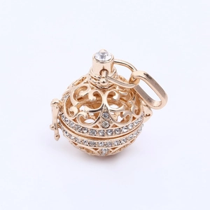 Détail d'un pendentif sphère dorée ajourée avec motifs et strass blancs brillants