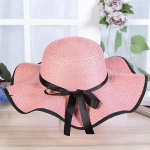 Close-up of pink woven straw hat featuring an elegant black ribbon bow detail