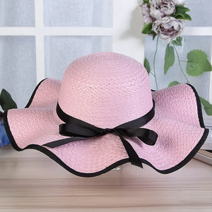 Detailed texture of pink woven straw hat with black bow and scalloped edge detail