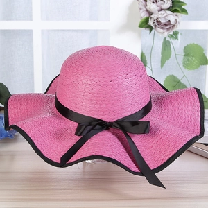 Detailed close-up of rose pink woven straw hat with wide wavy brim and black bow ribbon