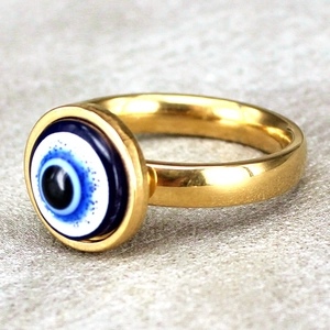 Golden stainless steel evil eye ring with blue enamel inlay on a grey textured background