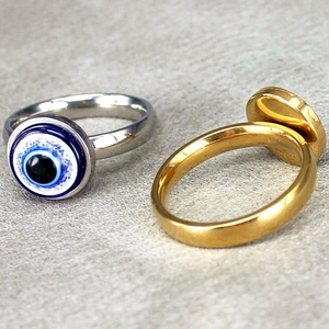 Silver and gold evil eye stainless steel rings with blue eye motif on grey background