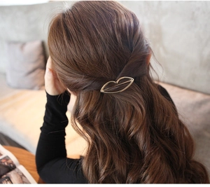 Detail of a golden lip-shaped hollow metal hair clip worn on wavy brown hair